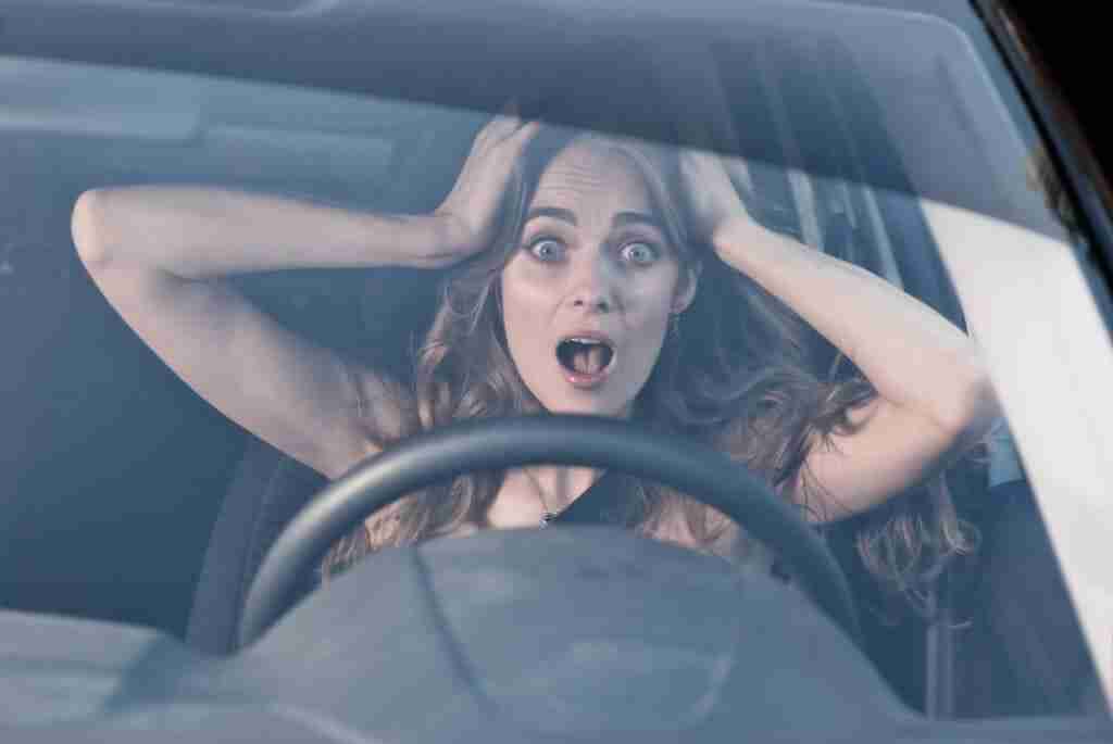 Young woman with hands on eyes sitting scared in car