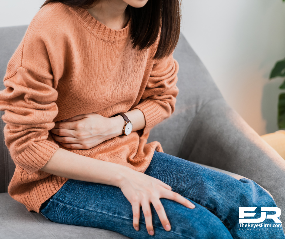 Woman sitting on a couch holding her stomach in pain, possibly experiencing stomach pain after a car accident – The Reyes Firm